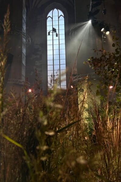 Wnętrze gotyckiego kościoła z zieloną, leśną instalacją.