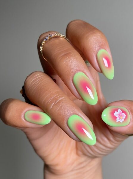 Różowo-zielony manicure z białym kwiatem na kciuku.