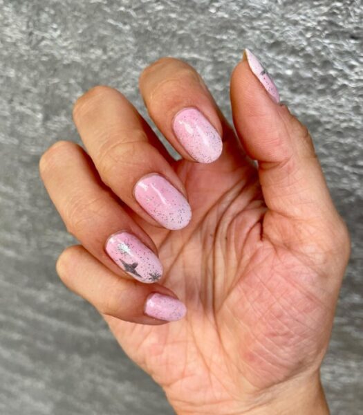 Jasny manicure z połyskiem i srebrnymi gwiazdkami.