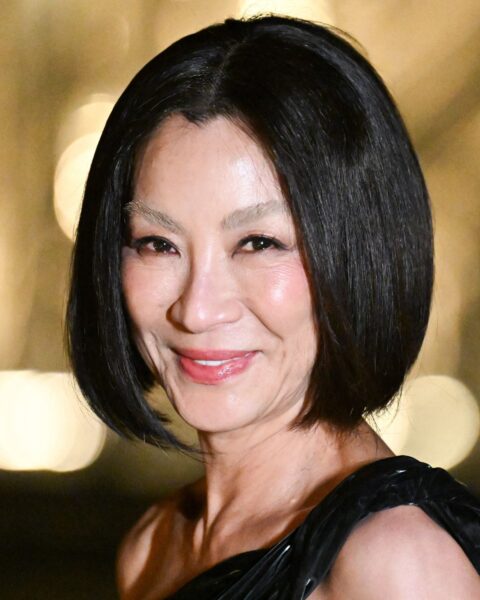Zdjęcie aktorki Michelle Yeoh. Ma krótkie, ciemne włosy na boba. Ubrana jest w wieczorową, czarną sukienkę z jednym ramiączkiem. Ma rozjaśniane, białe brwi.