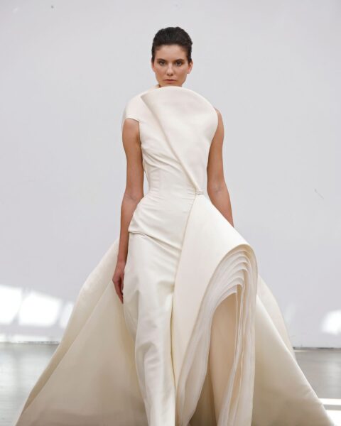 Co to jest haute couture? Zdjęcie z pokazu haute couture Rami Al Ali Couture AW25. Jest na nim modelka z ciemnymi włosami ubrana w kremową, wieczorową suknię o zdekonstruowanym fasonie.