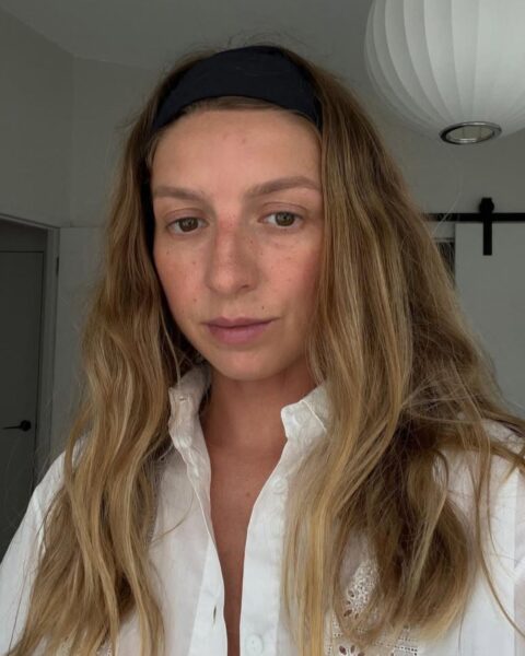Zdjęcie portretowe kobiety. Zrobiła sobie selfie. Ma długie, blond rozpuszczone włosy. Na głowie nosi czarną opaskę. Jest ubrana w białą koszulę z ażurowymi wzorami.