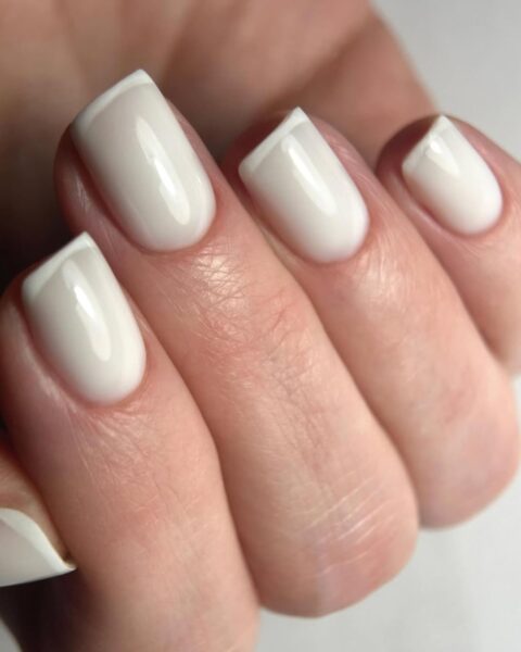Zdjęcie dłoni ze zbliżeniem na długie, kwadratowe paznokcie z french manicure w kolorze mlecznobiałym.