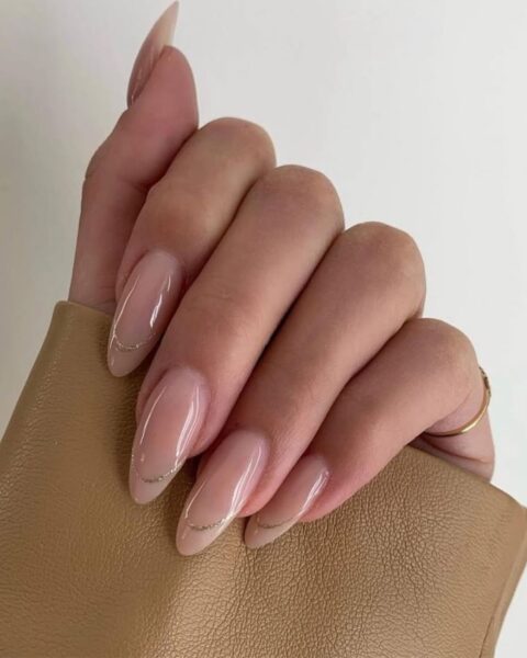 Zdjęcie dłoni z długimi, migdałowymi paznokciami w kolorze nude z french manicure z brokatową końcówką.