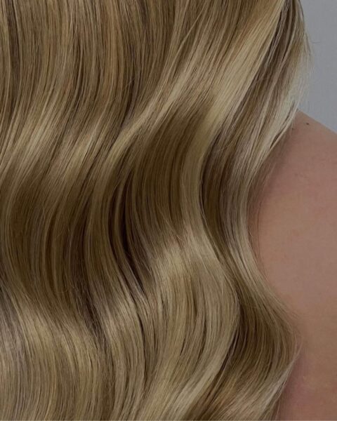 Zdjęcie ze zbliżeniem na włosy po zabiegu glass hair. Mają kolor blond, falują się i lśnią mocnym blaskiem. Opadają na ramiona.