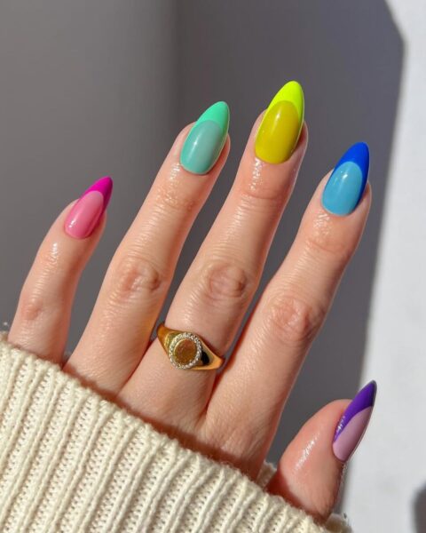 Zdjęcie dłoni ze zbliżeniem na długie, migdałowe paznokcie. Są pomalowane w stylu jelly french manicure. Każdy paznokieć ma inny kolor. Paznokcie mają efekt jelly, ale końcówki są matowe, neonowe.