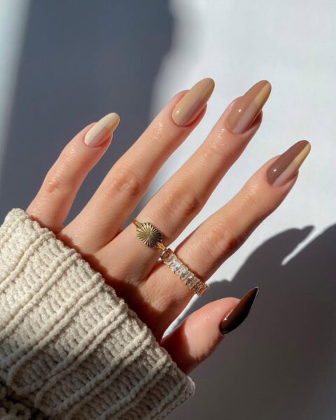 Zdjęcie dłoni ze zbliżeniem na karmelowy manicure: karmel połączony jest z beżem. Na palcach widać dwa pierścionki.