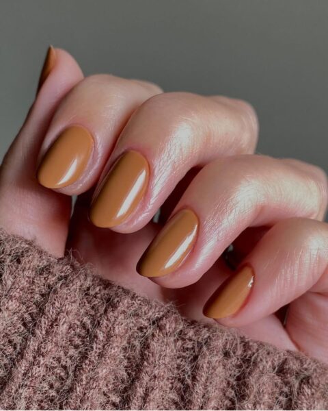 Zdjęcie dłoni z długimi, owalnymi paznokciami w kolorze karmelowym. Dłoń pozuje tak, by prezentować manicure.