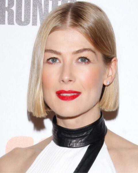 Zdjęcie aktorki Rosamund Pike, która ma krótkie włosy dla 50-latki, czyli prostego boba. Ma na sobie biały top z czarną stójką.