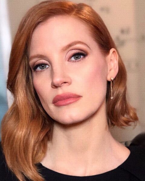Zdjęcie aktorki Jessici Chastain. Ma krótkie, rude włosy o asymetrycznej formie. Z jednej strony są dłuższe, przedziałek z boku. W uszach ma złote, wiszące kolczyki.
