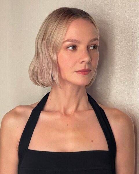 Zdjęcie aktorki Carey Mulligan w krótkiej fryzurze typu jawline bob w kolorze blond. Aktorka jest ubrana w czarny top wiązany na ramionach.