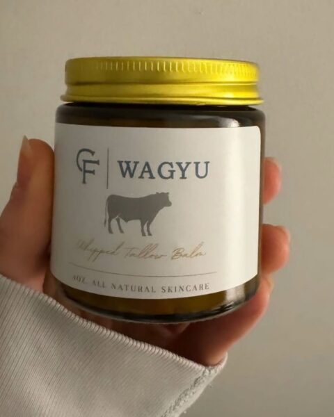 Zdjęcie dłoni trzymające słoik z łojem wołowym z wagyu, przeznaczonym do stosowania na twarz.
