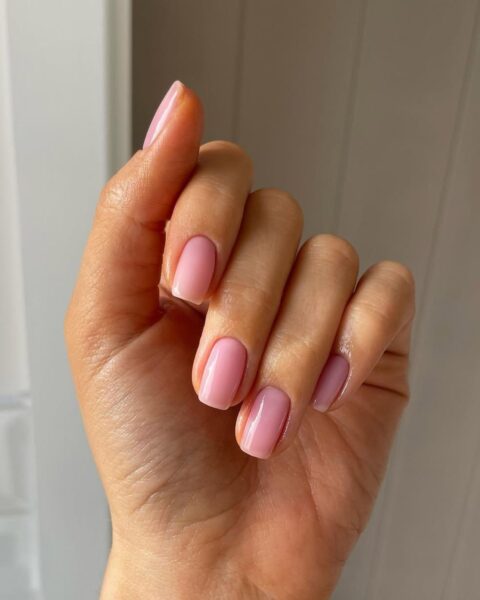 Zdjęcie dłoni ze zbliżeniem na średniej długości kwadratowe paznokcie w kolorze pink nude.
