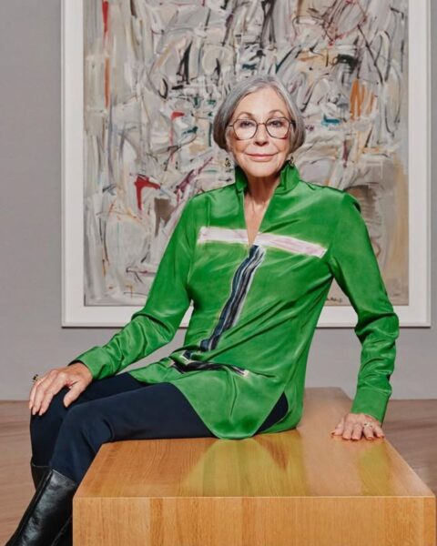 Zdjęcie Alice Walton. Siedzi na ławce w galerii, a za nią widać abstrakcyjny obraz. Ubrana jest w zieloną bluzkę, granatowe spodnie, czarne kozaki. Ma krótkie, siwe włosy oraz okulary korekcyjne na nosie. Ma długie, pomalowane na kolor nude paznokcie, taki typowy manicure najbogatszych kobiet świata.