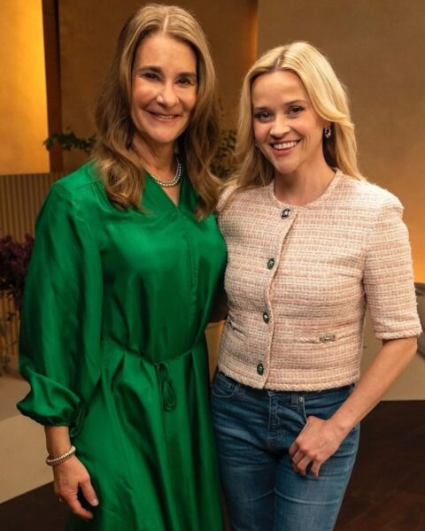 Na zdjęciu jest Melinda French Gates i Reese Witherspoon. Gates ma rozpuszczone włosy, ubrana jest w zieloną sukienkę. Obok Witherspoon w jeansach, różowym żakiecie z krótkim rękawem i okrągłym dekoltem. Tez ma rozpuszczone włosy. Obejmują się razem w studio telewizyjnym.