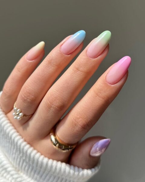 Zdjęcie dłoni ze zbliżeniem migdałowe paznokcie ozdobione wzorem ombre nails w pastelowych barwach. Na palcach widać złote pierścionki.