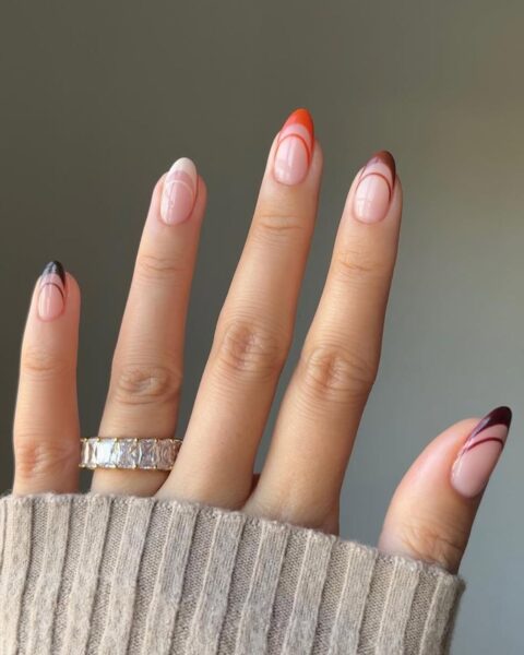 Zdjęcie dłoni ze zbliżeniem migdałowe paznokcie. Zdobi je podwójny french manicure w różnych kolorach. Na palcu serdecznym widać pierścionek z kryształem.
