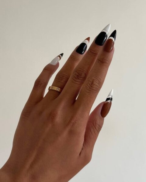 Zdjęcie dłoni z migdałowymi paznokciami. Są pomalowane na french manicure z graficznym french manicure w kolorze brązu, bieli i czerni. Na palcu serdecznym widać złotą obrączkę.