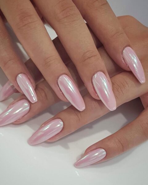 Zdjęcie dłoni ze zbliżeniem na długie paznokcie o kształcie balerina, w kolorze jasnego różu i efektem mirror nails. Dłonie układają się tak, by prezentować manicure.