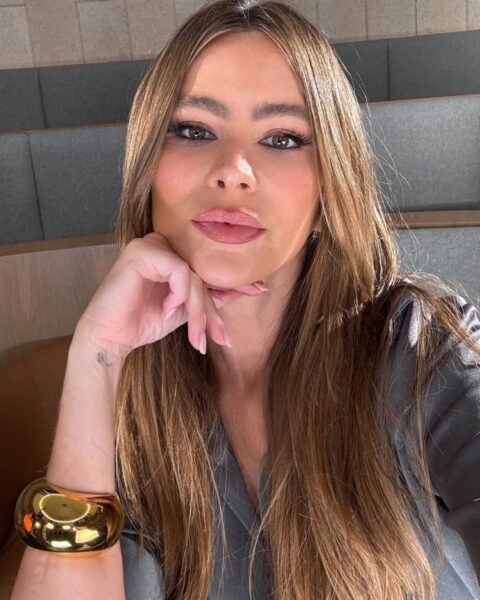 Na zdjęciu znajduje się Sofia Vergara, uznawana za jedną z najgorętszych aktorek po 50. Zrobiła sobie selfie. Ma długie, rozpuszczone na ramiona Włosy. Ubrana jest w szarą koszulę. Podpiera brodę o rękę, na nadgarstku widać masywną, złotą bransoletę.