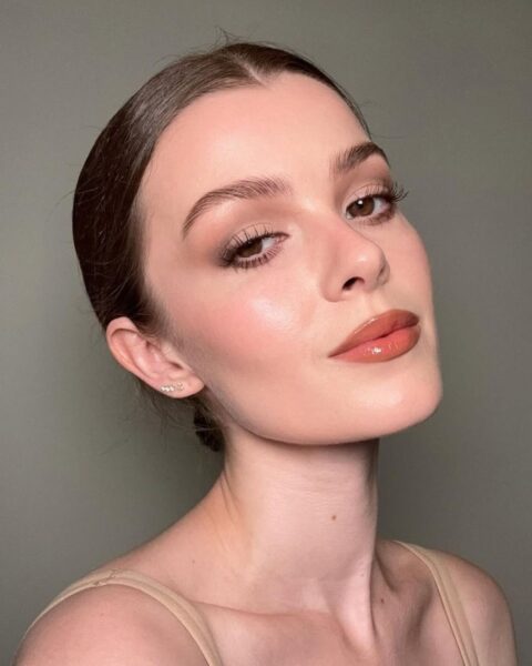 Zdjęcie wizażystki Ellise Ferguson. Pozuje półbokiem, odchylając głowę. Ma ciemne włosy gładko związane. Ubrana jest w beżowy top na cienkich ramiączkach. Na twarzy schludny, delikatny makijaż ze świeżym, rozjaśnionym spojrzeniem.