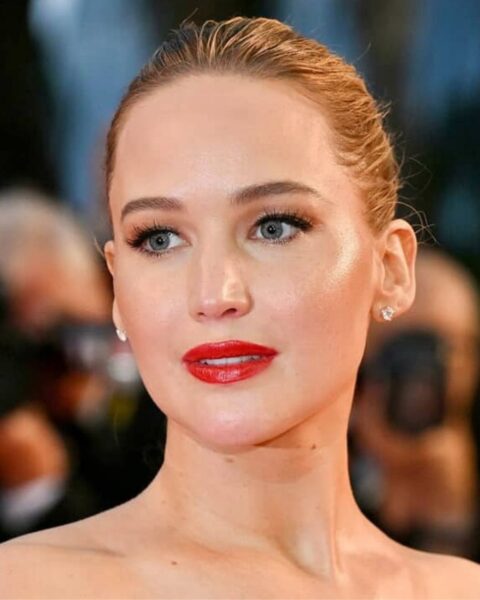 Zdjęcie aktorki Jennifer Lawrence, która ma blond włosy związane w kok. Makijaż z kreską i czerwonymi ustami. Ma modne, naturalne brwi.