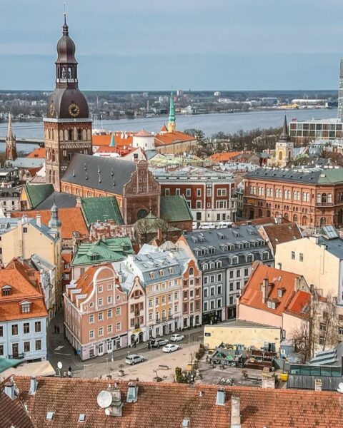 Widok na stare miasto w Rydze, w Łotwie, na dachy kamienic. Widać wieżę kościoła św. Piotra, a w tle rzekę Dźwina.