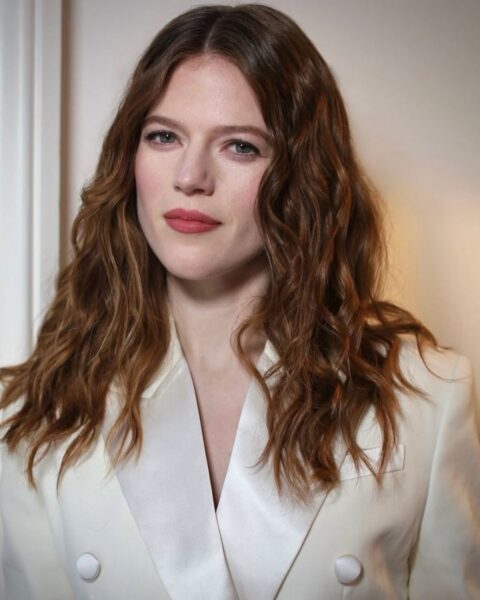 Zdjęcie, na którym jest aktorka Rose Leslie. Ma shy girl make up z różowymi ustami i policzkami. Jej rude, falowane włosy są rozpuszczone na ramiona. Ubrana jest w kremową marynarkę.