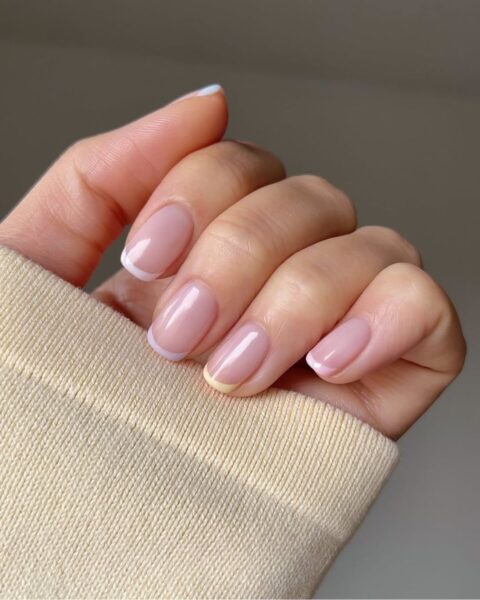 Zdjęcie dłoni ze zbliżeniem na średniej długości, kwadratowe paznokcie z french manicure z kolorowymi, pastelowymi końcówkami.