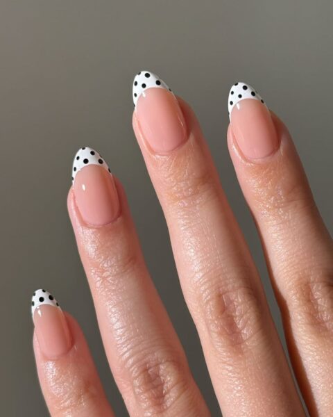 Zdjęcie dłoni ze zbliżeniem na migdałowe, długie paznokcie z french manicure, który ma kropki w stylu polka dots na białym pasku u brzegu paznokci.