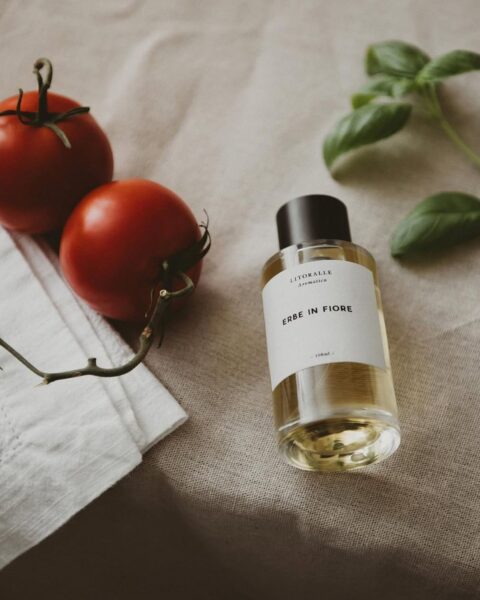Zdjęcie flakonu niszowych perfym slow fragrance leżących na beżowym obrusie w towarzystwie bazylii i pomidorów.
