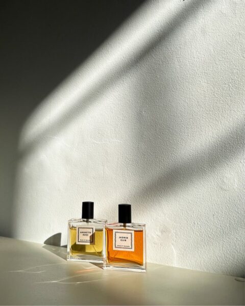 Zdjęcie dwóch flakonów perfum w stylu slow fragrance trend. Stoją na blacie, tuż pod ścianą i pada na nie światło słoneczne przez okno.
