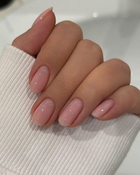 Zdjęcie dłoni ze zbliżeniem na mydlane paznokcie, tzw. soap nails w kolorze jasnego różu. Dłoń pozuje na tle umywalki. Prezentuje manicure.