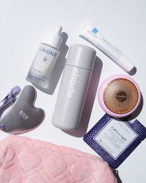 Zdjęcie białego blatu, na którym leży kosmetyczka oraz rozrzucone kosmetyki. Widać kamień gua sha, masażer, mgiełkę, serum, krem oraz maseczkę.