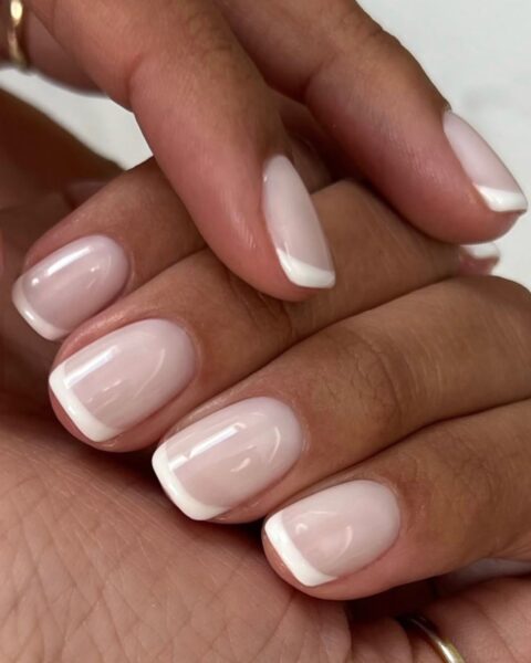 Zdjęcie dłoni ze zbliżeniem na średniej długości, kwadratowe paznokcie z milky french manicure, czyli z mlecznym kolorem bieli.