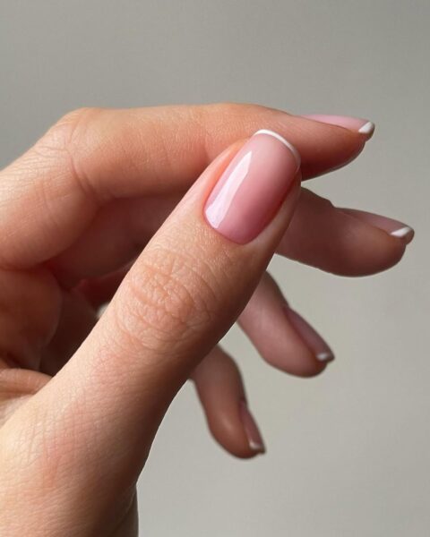 Zdjęcie dłoni ze zbliżeniem na micro french manicure z bardzo cienką, białą kreską. To bardzo elegancka stylizacja paznokci.