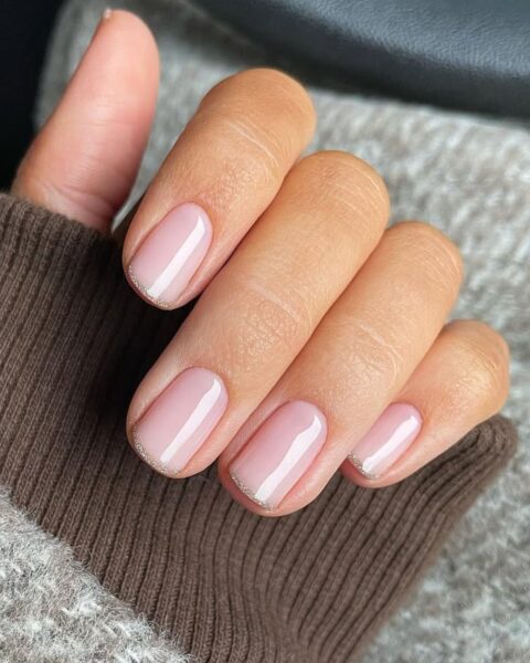 Zdjęcie dłoni ze zbliżeniem na french manicure z brokatową, bardzo cienką końcówką. Paznokcie są krótkie i mają kwadratowy kształt.