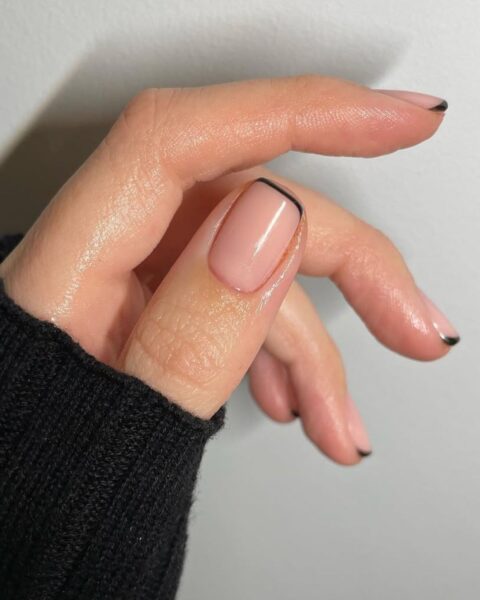 Zdjęcie dłoni ze zbliżeniem na krótkie, kwadratowe paznokcie z french manicure z czarną końcówką, bardzo cienką, w stylu micro french.