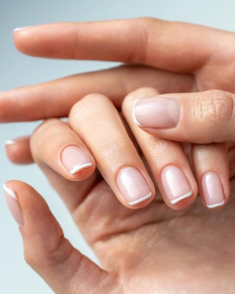 Zdjęcie dłoni ze zbliżeniem na krótkie, kwadratowe paznokcie z zaokrąglonymi brzegami i stylizacją french manicure, idealną do pracy w biurze.
