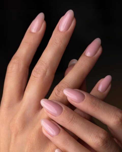 Zdjęcie dłoni ze zbliżeniem na manicure do pracy przy komputerze: średniej długości migdałki w kolorze różowego nude. Dłonie pozują na czarnym tle w taki sposób, by prezentować stylizację paznokci.