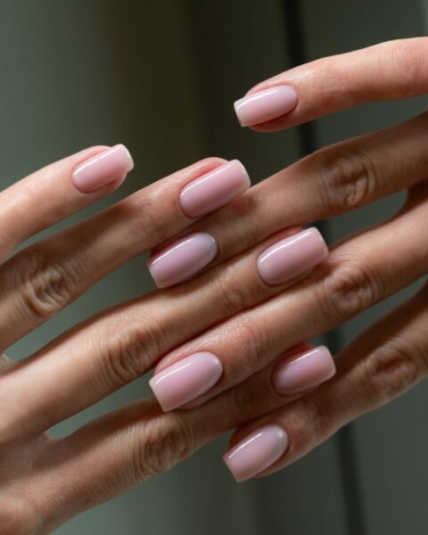 Zdjęcie dłoni i manicure, będącego przykładem, jakie paznokcie do pracy w biurze nosić: kwadratowe, średniej długości i w kolorze pink nude. Dłonie pozują tak, by prezentować manicure.