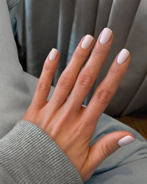 Zdjęcie dłoni i manicure z kwadratowymi paznokciami w kolorze mlecznej bieli.