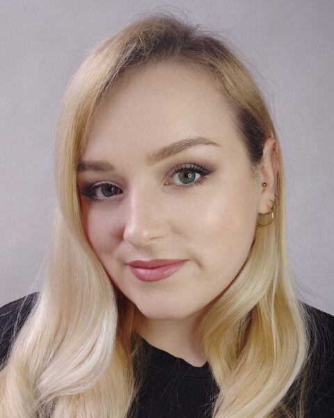 Blondynka o zielonych oczach z subtelnym makijażem, który rozświetla cerę. Perfekcyjne połączenie delikatnie podkreślonych brwi i ust w kolorze naturalnego, zgaszonego różu to esencja luksusowego makeup-no-makeup na dojrzałej cerze. Zbliżenie na technikę, która dodaje blasku i młodzieńczego wyglądu, idealne do eleganckich stylizacji dziennych.