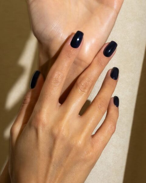 Zdjęcie ze zbliżeniem na zmysłowy manicure: kwadratowe paznokcie w sensualnym kolorze czarnym. Dłonie pozują tak, by prezentować manicure.