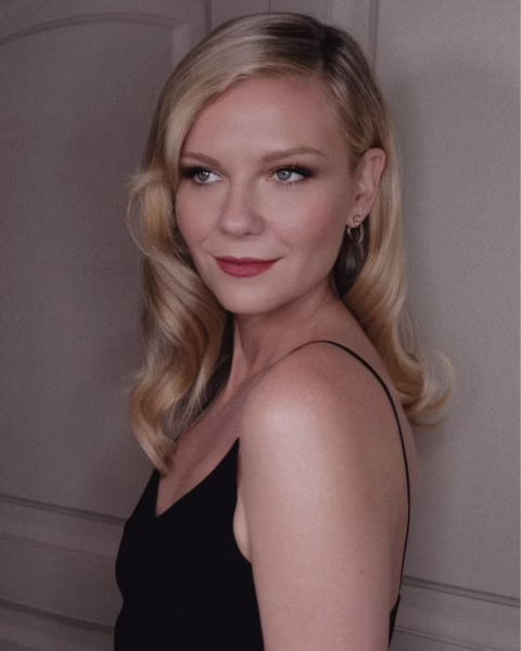 Portret Kirsten Dunst z blond włosami ułożonymi w fale, patrzącej w bok, ubranej w czarną sukienkę na ramiączkach.