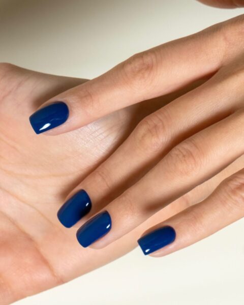 Zdjęcie dłoni z długimi, kwadratowymi paznokciami pomalowanymi na modny kolor: granatowy. Dłoń pozuje tak, by prezentować manicure.