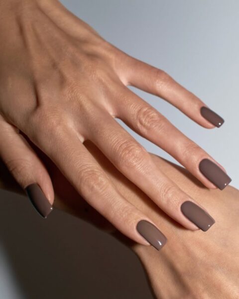 Zdjęcie dłoni ze zbliżeniem na modne paznokcie na jesień 2025: długie kwadraty pomalowane na kolor mocha mousse. Dłonie układają się tak, by prezentować manicure.