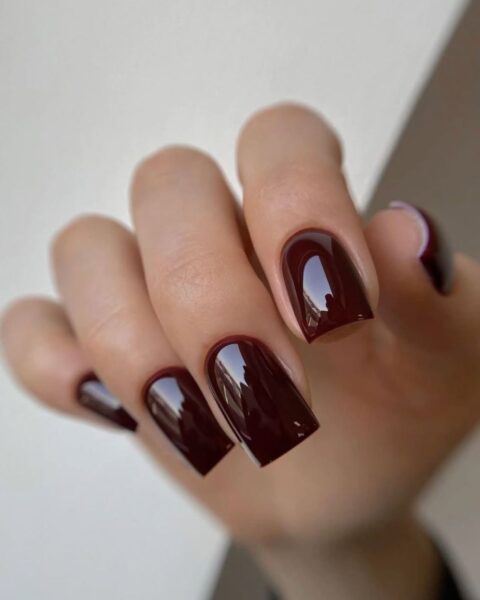 Elegancki manicure w głębokim odcieniu burgundu lub ciemnej wiśni. Długie paznokcie o kwadratowym kształcie z zaokrąglonymi krawędziami, pokryte lśniącym, błyszczącym lakierem.
