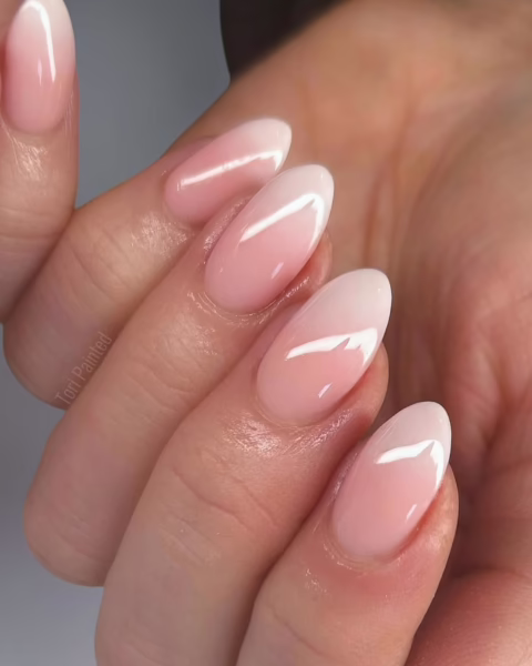 Zdjęcie dłoni ze zbliżeniem na długie, migdałowe paznokcie z gradientowym zdobieniem baby boomer. Dłoń pozuje tak, by prezentować manicure.