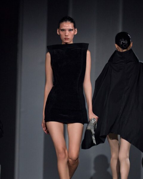 Geometryczna siła i klasa z pokazu Alexander Wang: modelka w futurystycznej czarnej mini sukience z mocno zaznaczonymi, ostrymi ramionami. Inspiracja dla kobiet ceniących architektoniczne formy i odważną elegancję.